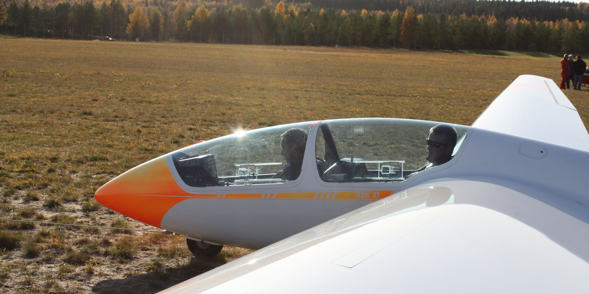 A two-seat glider on the field in low autumn sun, canopy open, ready for the next launch.